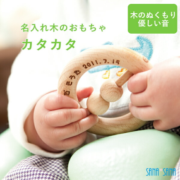 名前と日付を彫刻した木のカタカタを握る赤ちゃんの手